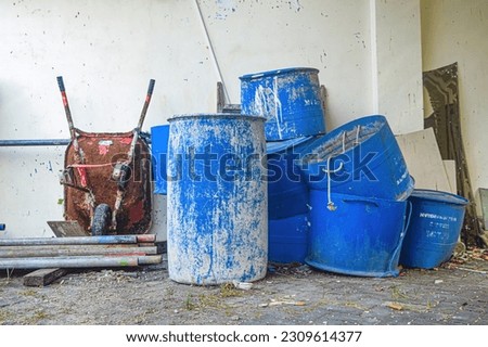 piles of unused water drums, trash cans, and wheelbarrows
