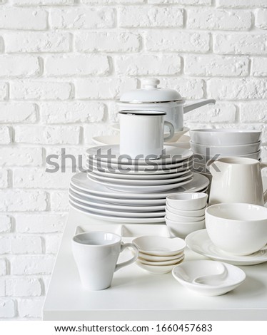 piles of white ceramic dishes and tableware on the table on white brick wall background with copy space