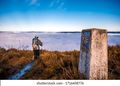 Pilgrim walking in Camino de Santiago, over a sea of clouds in the middle of the nature. We can see the icon of the shell.