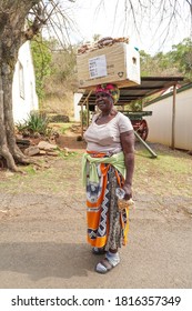 Pilgrims Rest,South Africa - August 06,2019: black African female street vendor carries her box of nuts on her head and turns to look at the camera making eye contact for a portrait concept daily life