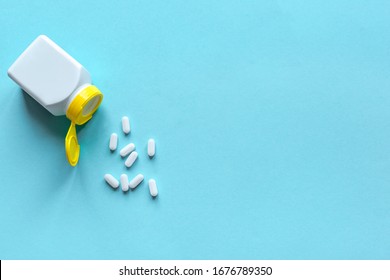 Pill Bottle And Pills On Blue Background, Top View, Copy Space. Medicine And Pharmacy Concept. Vitamins Or Generic Tablets.