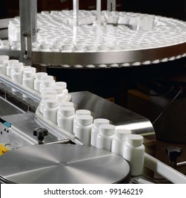 Pill Bottles Going Through The Pill Counter And Labeling Machinery In A Pharmaceutical Processing Facility.