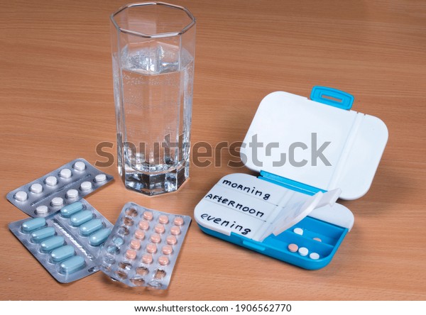 Pill box daily take medicine with pills, tablets\
and glass of water. Drugs use for treatment. Medication in medical\
clinic on wooden table
