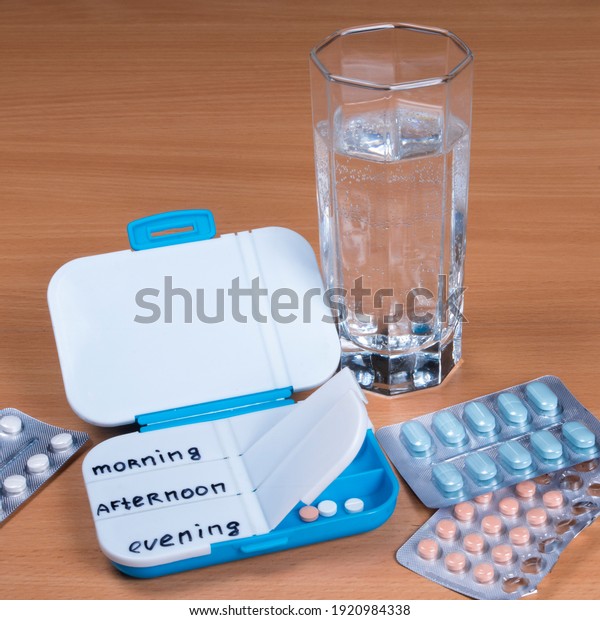 Pill box daily take medicine with pills,\
tablets and glass of water. Medication in medical clinic on wooden\
table. Drugs use for\
treatment.