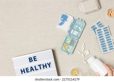 Pill Box Daily Taking Medicine, With Tablets And Capsules. Drugs, Medication As Alternative Medicine For Treatment And Good Health. Medicine Dose Box With Pills On Table, Text Be Healthy On Light Box