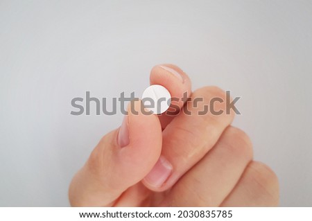 Pill in hand. Close up to vitamin or medicine tablet between two fingers. Small round white pill. Diet supplement or drug concept holden in hand. Brigh background. Pharmaceutical product. Pain killer.