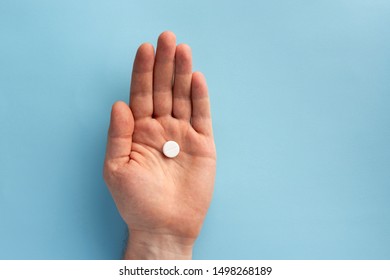 Pill in the male hand, on blue background. Flat lay.