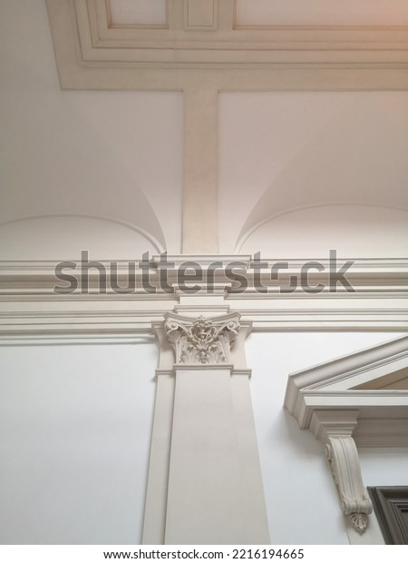 Pillar with corinthian order under wall molding\
and ceiling frame. Classical architecture fragment. Architectural\
detail. Gypsum fretwork pilaster. Modern interior in ancient Greek\
or Roman style.