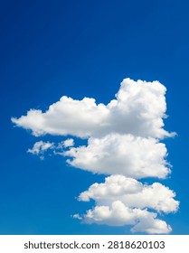 pillar of several fluffy white clouds lined up vertically in the center of the frame against a rich clear blue sky
