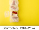 Pillbox closeup. Pills and supplements on yellow background, top view. Capsules in daily organizer. Weekly pill organizer and pill. Clear plastic pill container and medications. High quality photo