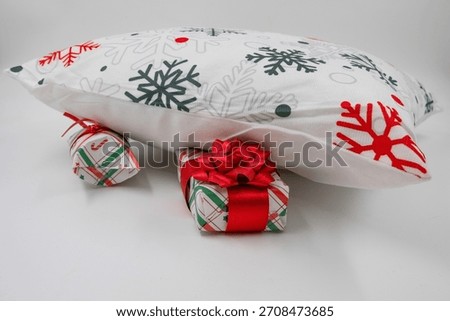 Pillow with festive snowflake pattern resting above wrapped Christmas gifts on white background