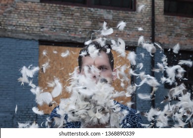 Pillow Fight Outdoor. A Man Having Fun During A Pillow Fight. There Are Feathers In The Air