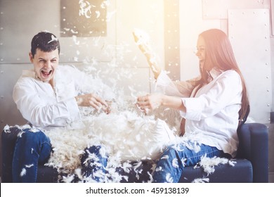 Pillow Fight. Young Happy Pregnant Family Have Fun With Fluffy Feathers From Pillow. Man And Woman Dressed In Jeans And White Shirts. Vintage Color Effect.