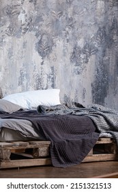 Pillows and mattress on a makeshift pallet bed, covered with gray blankets. The bed is against the wall with old plaster