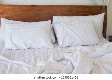 Pillows on the bed with white bedlinen and wooden bedhead on the sunny morning
