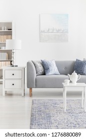 Pillows on grey couch next to lamp on cabinet in elegant living room interior with poster. Real photo