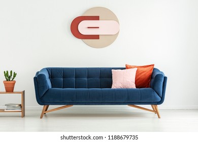 Pillows On Navy Blue Couch Next To Plant On Table In White Living Room Interior With Poster. Real Photo