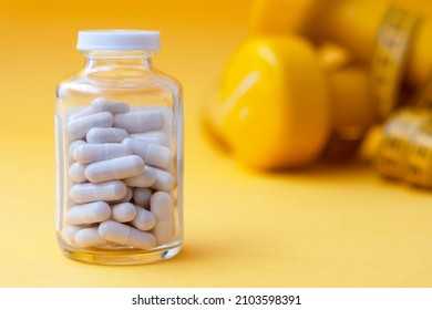 Pills capsules in a glass jar close-up with dumbbells and a centimeter tape in the background. The concept of weight loss, sports, fitness, fat burner, vitamins, sports nutrition.