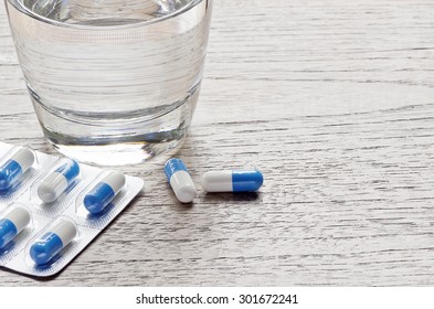 Pills capsules medicine and glass of water on wooden background.