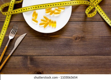 Pills Or Dietary Supplement For Weight Loss. Treatment Of Obesity. Treatment Of Anorexia. Gold Pills On Plate Near Measuring Tape On Dark Wooden Background Top View.