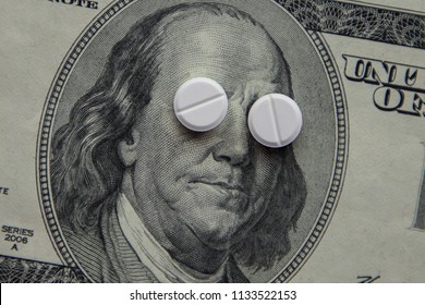 The Pills Lie In Place Of The Eyes, On A Bill Of One Hundred Dollars Close-up. The Concept Of Insurance Medecine, Insurance, High Cost, High Cost Of Drugs.