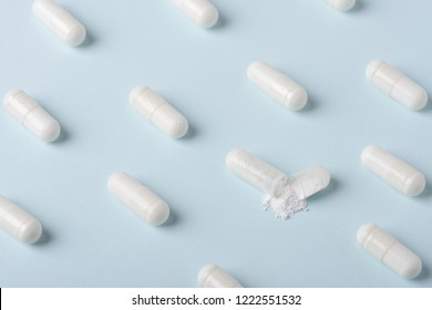 Pills pattern with one capsule open and white powder spilling over blue background