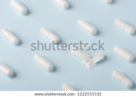 Pills pattern with one capsule open and white powder spilling over blue background