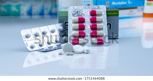 Pills in pharmacy shop. White tablets pills on\
blurred capsule in blister pack and white tablets pills in pack\
near drug box package. Pharmacy products. Pharmaceutical industry.\
Drugstore business.