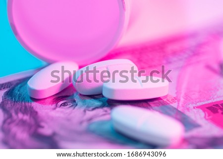 Pills and pill bottle on top of stack of one hundred dollar bills on neon dutone backgroud