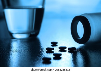 Pillen, Plastikflasche und Glas Wasser auf dem Tisch in Kontrastlicht