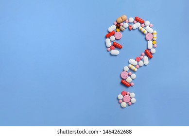 A lot of pills scattered on a blue background. A question mark laid out of pills. Counterfeit medicinal products. Empty space to insert text