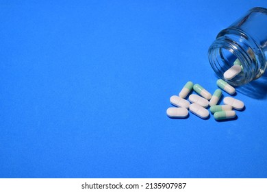 Pills Scattered On Blue Background And In A Small Glass Container.