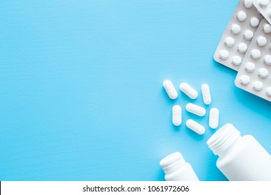 Pills spilled out of white bottle on blue background. Mock up for special offers as advertising or other ideas. Medical, pharmacy and healthcare concept. Copy space. Empty place for text or logo. 