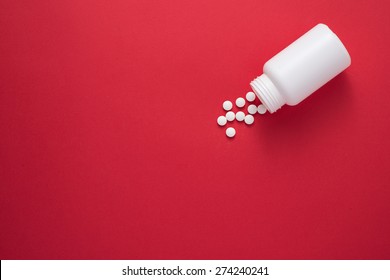 Pills spilling out of pill bottle and isolated on red. Top view with copy space. Medicine concept