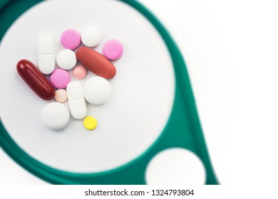 pills under a magnifying glass on the white background. Testing, verification and determining pharmaceutical counterfeiting or fake 