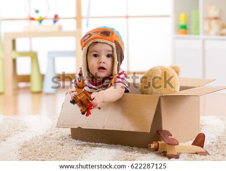 Pilot aviator baby boy with teddy bear toy and planes plays in cardboard box