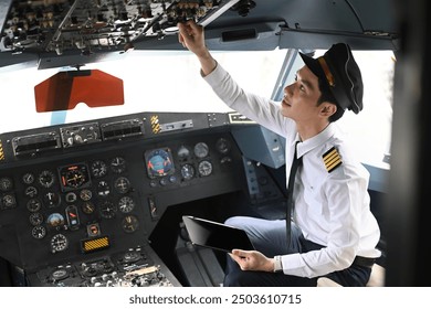 Pilot with digital tablet sitting in cockpit and adjusting controls on the overhead panel. - Powered by Shutterstock