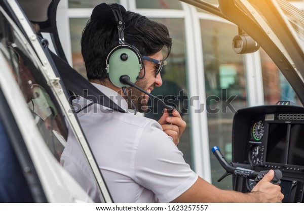 Pilot with\
headset starting the controls in the private helicopter. Helicopter\
pilot sitting in the\
cockpit.