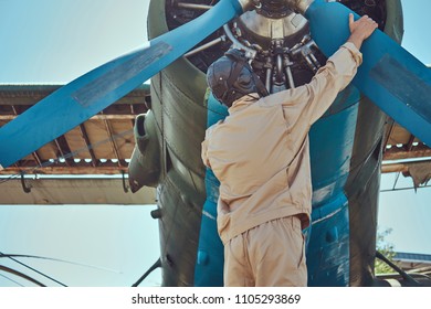 Pilot Or Mechanic In A Full Flight Gear Checks The Propeller Of His Retro Military Aircraft Before A Flight.