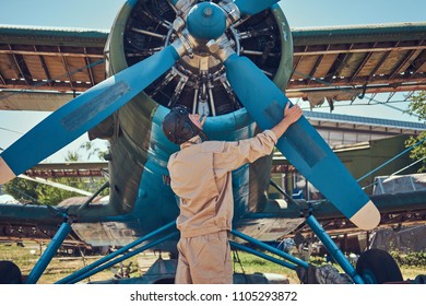 Pilot Or Mechanic In A Full Flight Gear Checks The Propeller Of His Retro Military Aircraft Before A Flight.