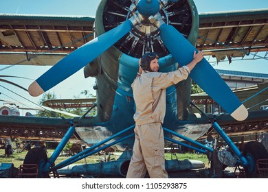 Pilot Or Mechanic In A Full Flight Gear Checks The Propeller Of His Retro Military Aircraft Before A Flight.