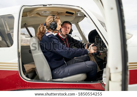 Pilot in training and flight instructor in the cockpit of an airplane. Female young pilot with headphones preparing to fly. He is sitting next to the female instructor attending to her explanations.