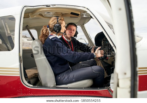 Pilot in training and flight instructor in\
the cockpit of an airplane. Female young pilot with headphones\
preparing to fly. He is sitting next to the female instructor\
attending to her\
explanations.