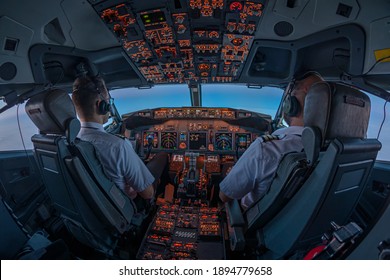 Pilots in the cockpit of jet commercial airplane during the flight with first rays of the warm sunrise entering through the flight deck window