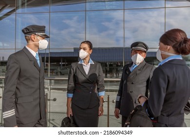 Pilots And Flight Attendants In Protective Masks Talking Near The Terminal