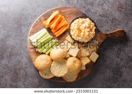 Pimento or pimiento cheese is a spread made of cheese, mayonnaise and pimientos and served on crackers and vegetables closeup on the wooden board on the table. Horizontal top view from above
