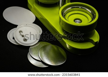 Pin button making green machine over a black background. Blank badges on the frame.