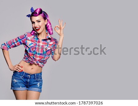 Pin up girl. Portrait photo of excited happy smiling woman showing ok sign gesture. Retro and vintage studio concept. Grey color background. Copy space for some text. 