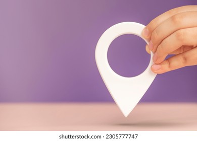 Pin icon or travel nautical map. GPS direction indicator. A hand holds a location sign on a purple background. Laying a route, finding a location. copy space. - Powered by Shutterstock