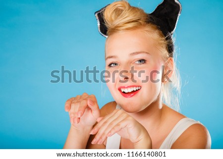 Pin up and retro style. Young smiling woman with black ears pretending mouse on head on blue background. Studio shot.